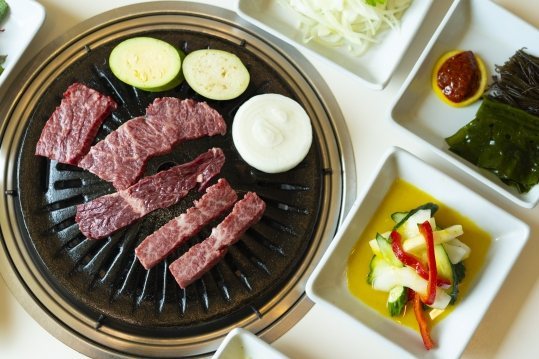 위에서 본 불판 위 생 한우와 호박·양파, 둘레의 양파채·초장·해초·절임채소