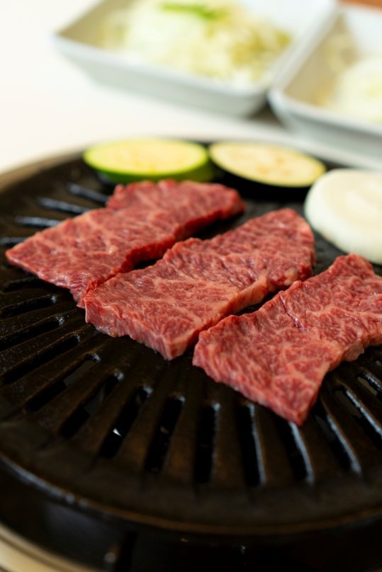 불판 위에 올린 마블링 있는 생 한우 세 점과 호박·양파